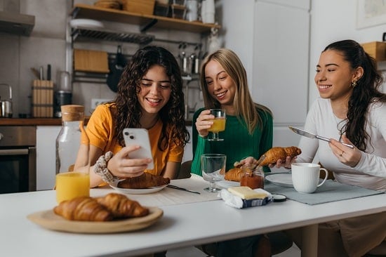 A group of three women is having breakfast with croissants and orange juice
