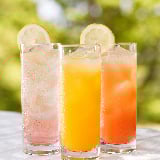 Three glasses containing different fruit juices sit on a table.