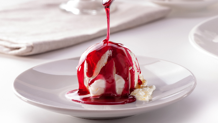 A scoop of ice cream with a red sauce being poured over it on a plate