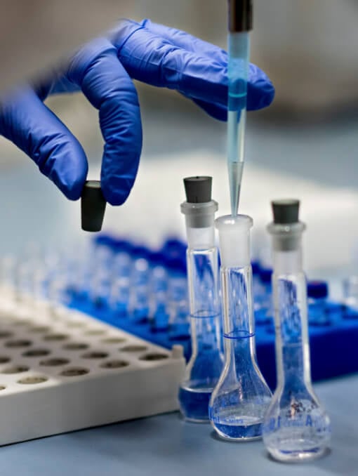 A hand holding a pipette over test tubes
