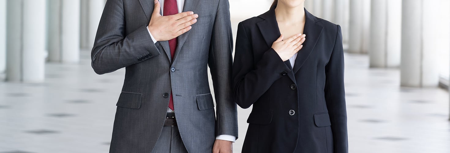 Man and woman in suits with hands over hearts