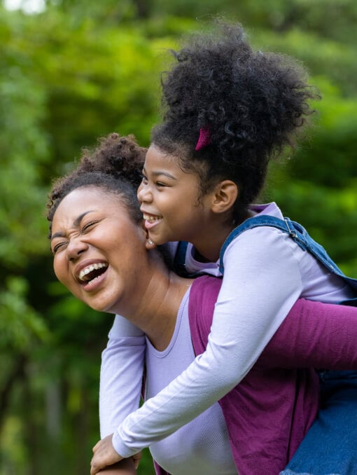 A person smiling while giving a piggyback ride to a child