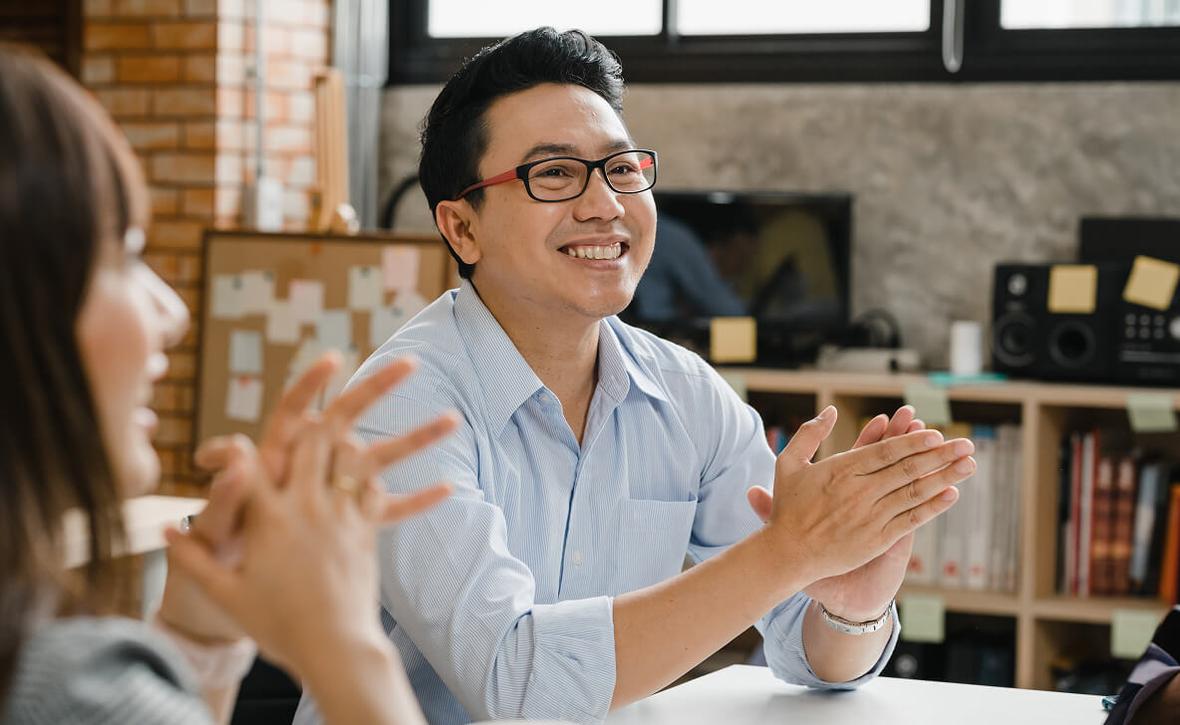 A smiling person holds their hands together in an office setting
