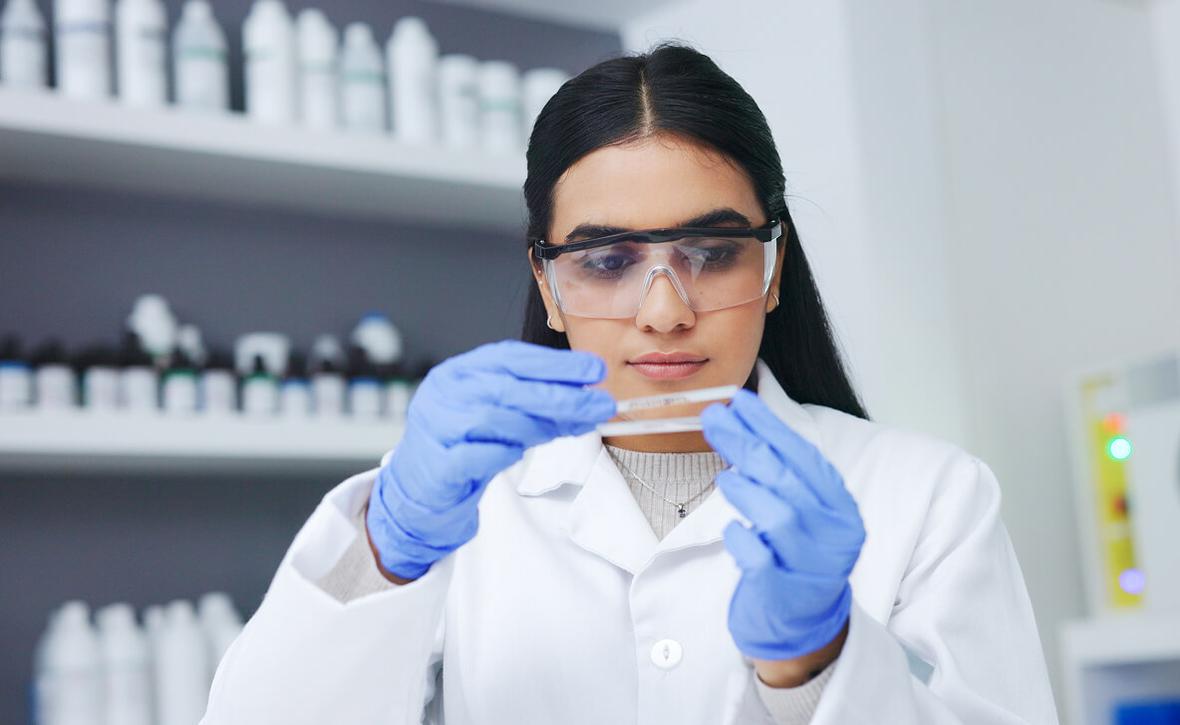 A person wearing lab goggles and gloves works in a lab setting