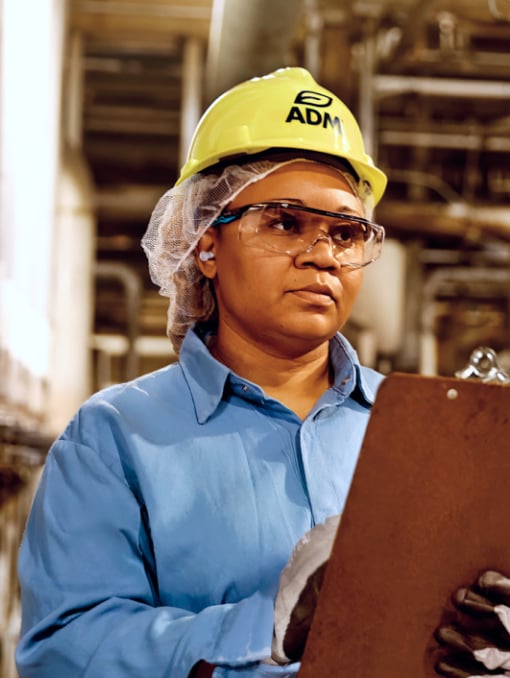An ADM employee wearing a hardhat and safety glasses, writing on a clipboard
