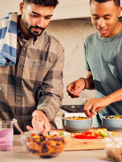 Two people preparing food in a kitchen with ingredients in bowls and on a cutting board