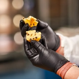 Closeup of a person wearing black gloves and breaking apart a muffin