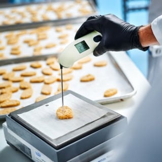 Closeup of a person wearing a black glove inserting a food thermometer into a plant-based chicken nugget