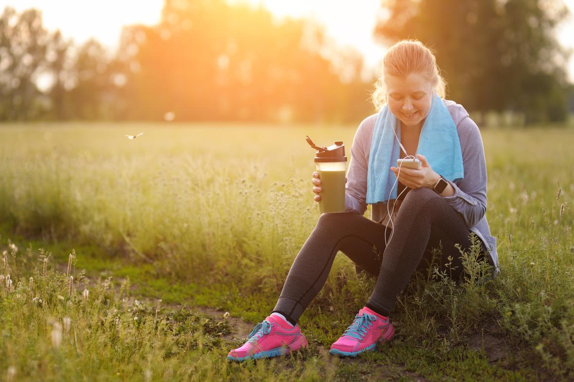 A woman sitting by a grass running path enjoying a sports drink