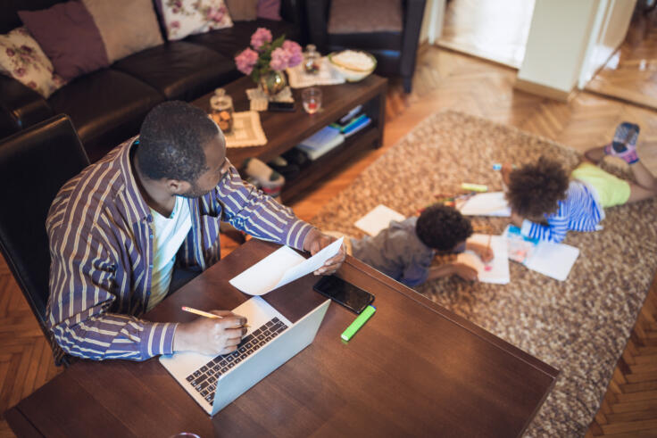 Father working from home while his two children are playing in the living room GettyImages 1156715165[1]