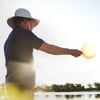 A man wearing a blue shirt with the ADM brand on the left arm is feeding the fishes, amidst a background containing additional fish farms, including clear blue skies and green coloured water.