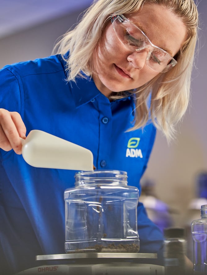 A female scientist is seen pouring contents from a small handheld shovel containing ingredients for aquaculture.