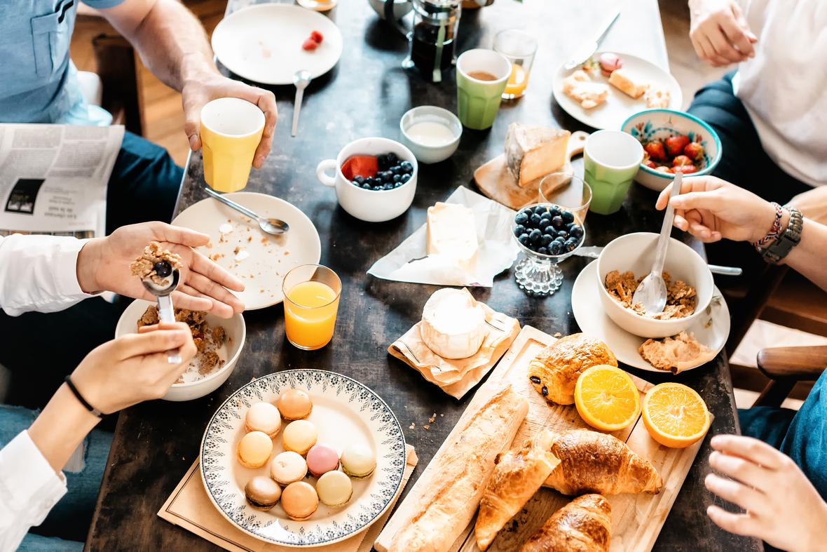 Group of people eating breakfast together with baked goods, cereal and fruit on the table