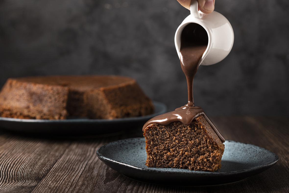 Chocolate sauce being poured onto a slice of chocolate cake