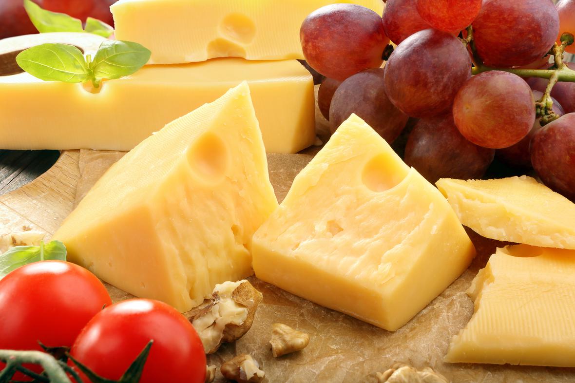Pieces of hard cheese on a serving tray with fruit and vegetables around