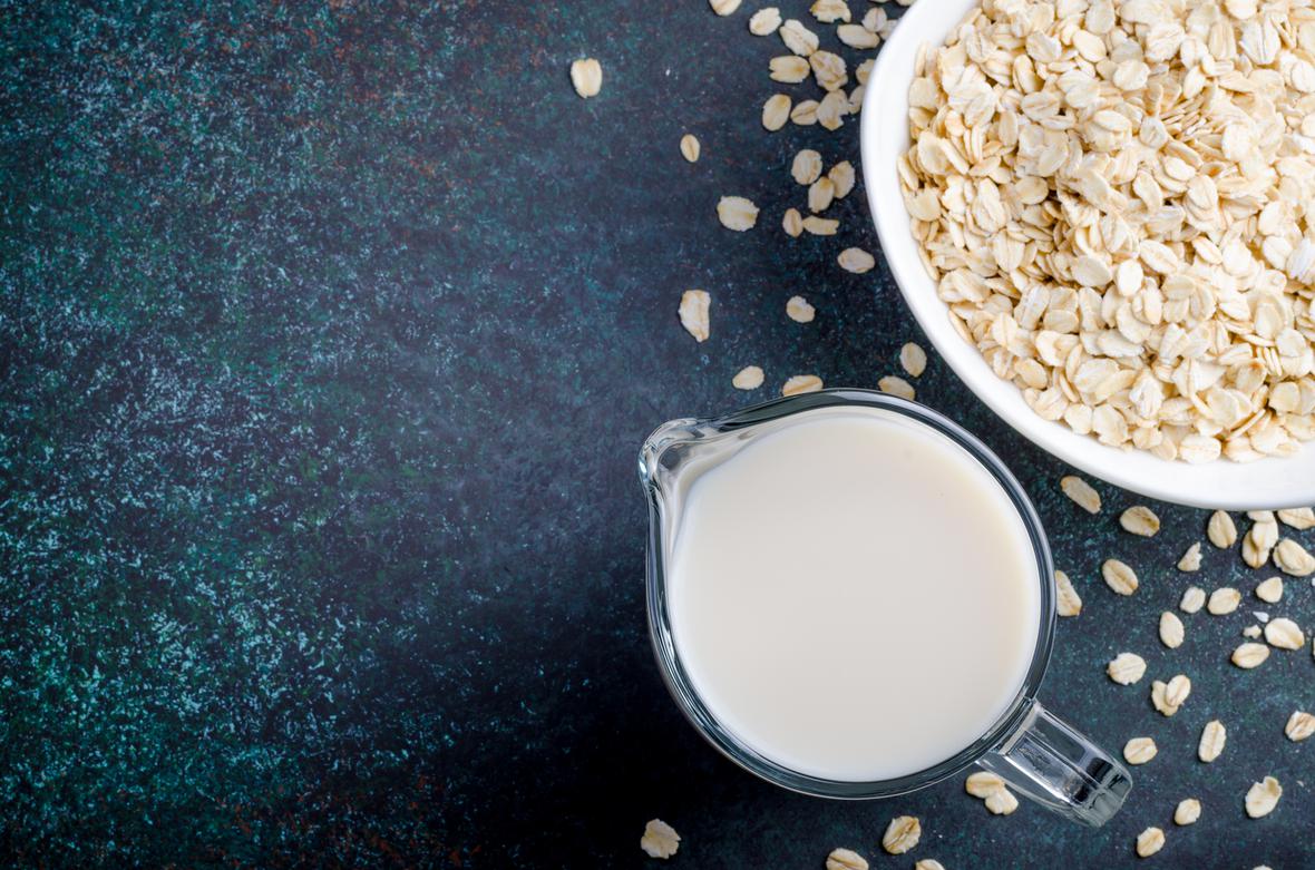 Glass measuring cup full of plant-based milk next to a bowl of oats