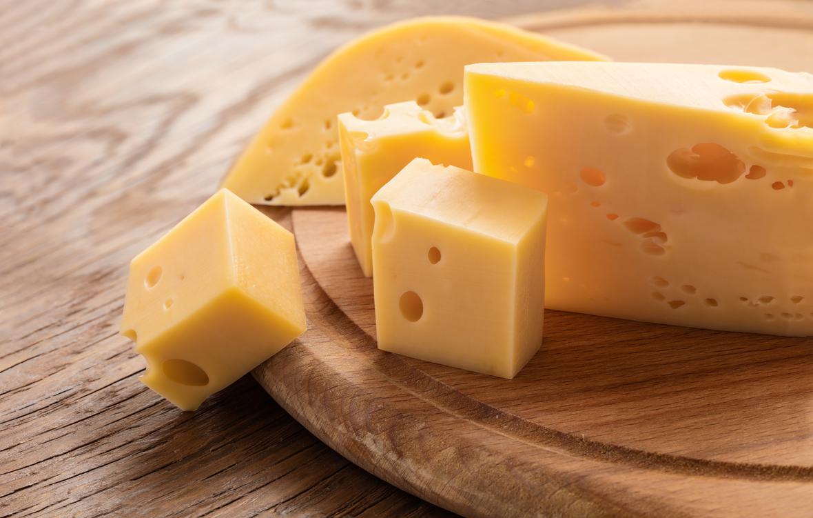 A large slice of cheese with smaller cubes on a wooden serving dish