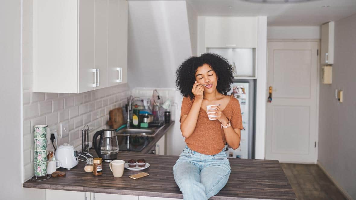 Woman sitting on kitchen island eating yogurt