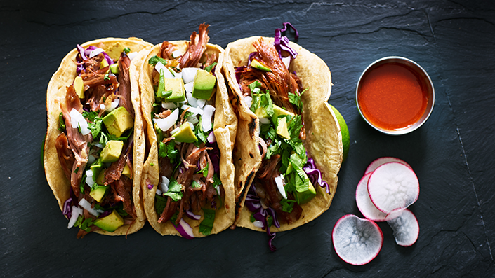 Three Tacos with alternative meat shown on a black granite surface, sauce and radish on the side
