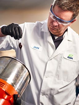 Man wearing safety equipment and white ADM lab coat examining product
