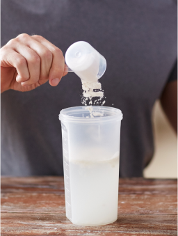 A close-up of a man pouring protein powder into a shake canister in his kitchen.