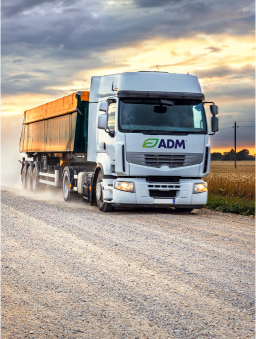 A large ADM transport truck driving on a dirt road at dusk.