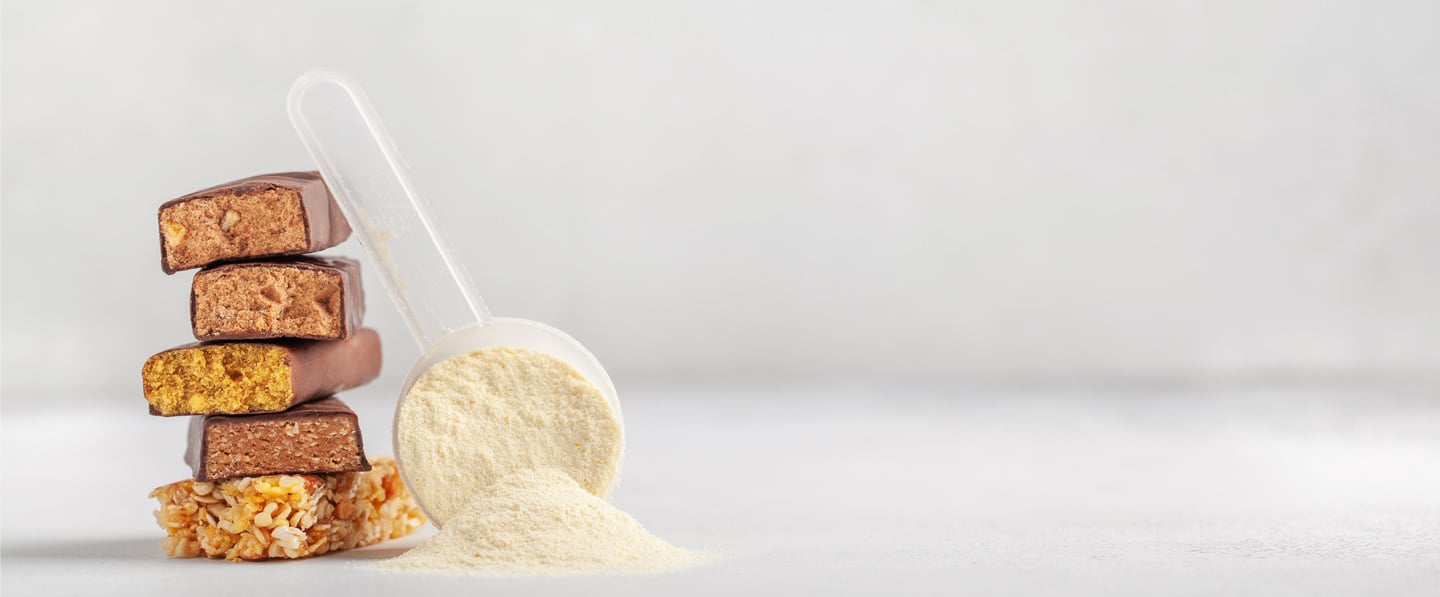 A plastic scoop of protein powder leaning up against a stack of cut pieces of a protein bar.