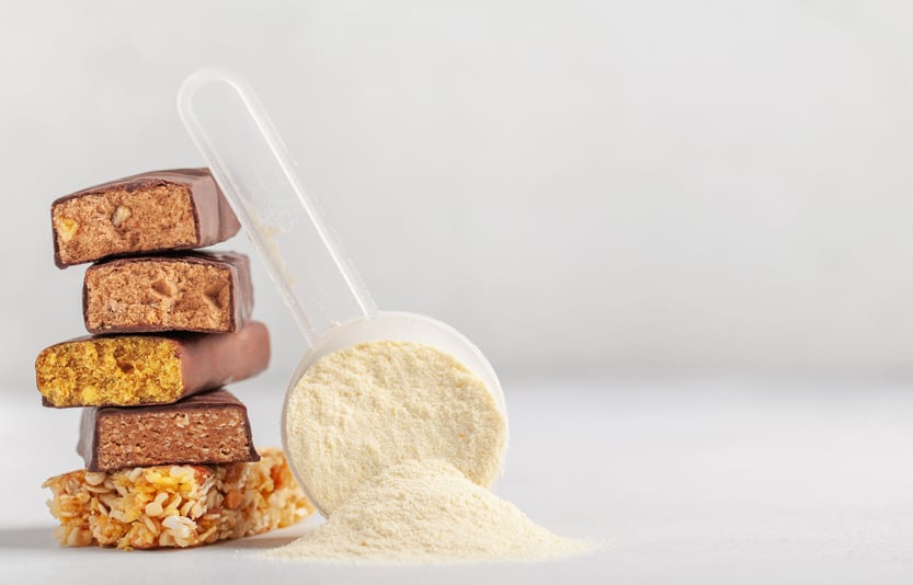 A plastic scoop of protein powder leaning up against a stack of cut pieces of a protein bar.