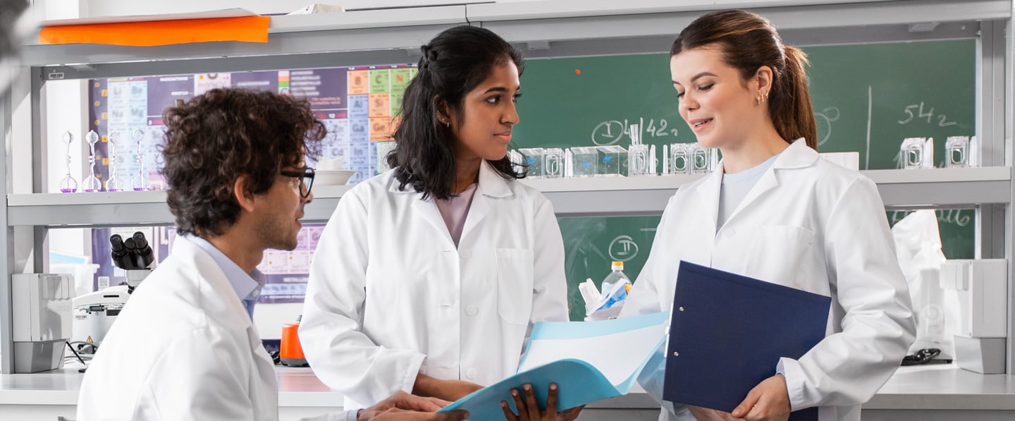 A group of three food scientists gathered in their lab to discuss something on a sheet of a paper they are all looking at.