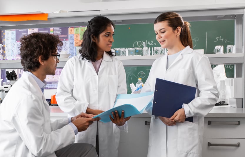 A group of three food scientists gathered in their lab to discuss something on a sheet of a paper they are all looking at.