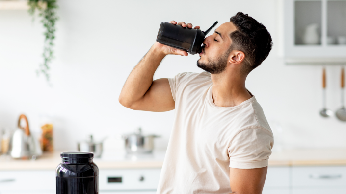 A man drinking a nutritional shake in his kitchen.