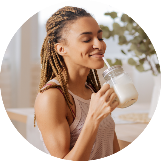 A woman enjoying a plant-based beverage in a cup with a straw.