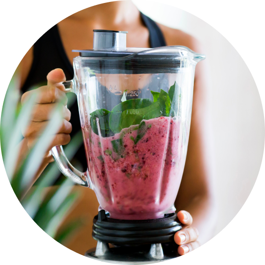 A close-up of a woman making a smoothy of berries and spinach in a blender.