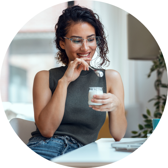 A woman sitting at a table enjoying a yogurt in a small glass container.