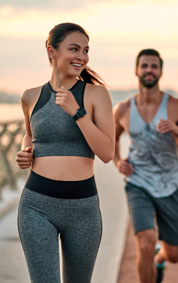 A woman and a man running outside with the woman looking back and smiling at the man who is slightly behind her.