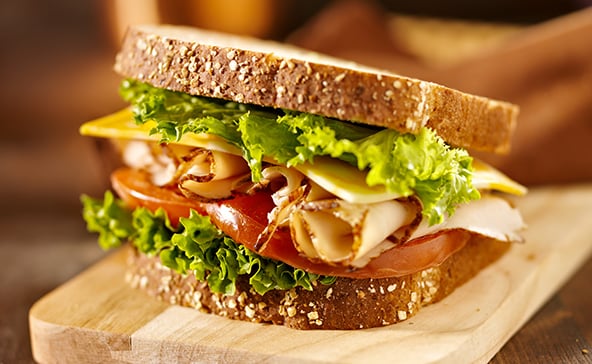 A deli sandwich with sliced turkey on a wood platter