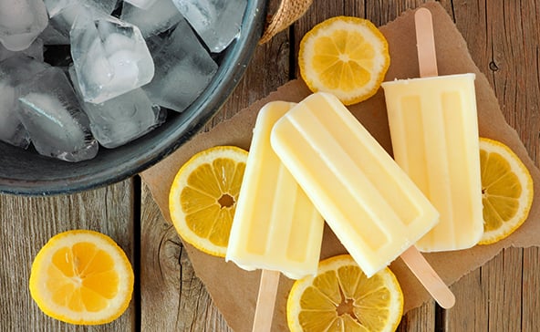 Three frozen lemon popsicles on a table with lemon slices surrounding them