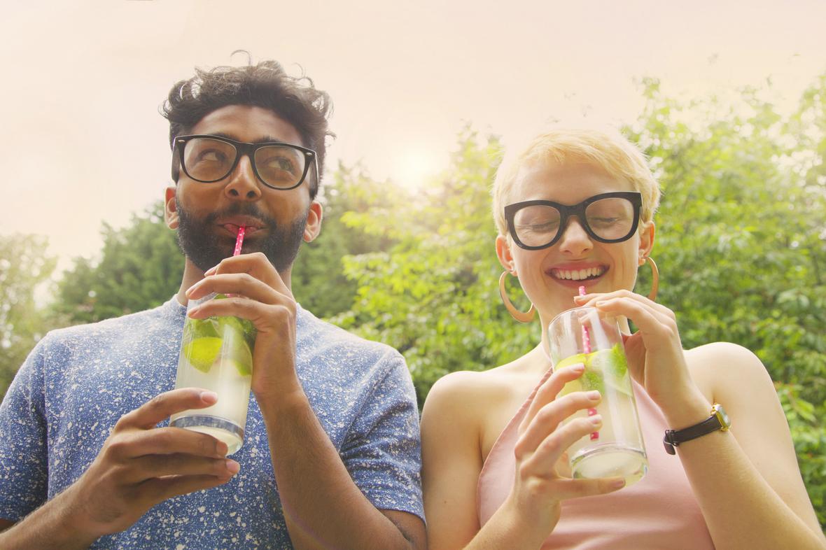 Cheerful couple drinking lemonade on a sunny day with trees in the background