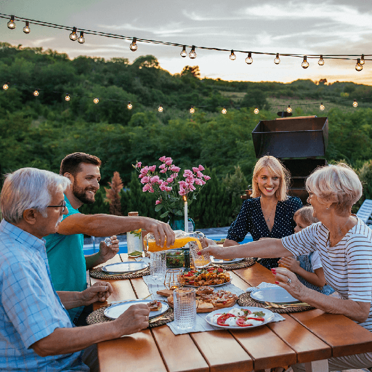 A family enjoying a meal outdoors at a picnic table, surrounded by greenery.