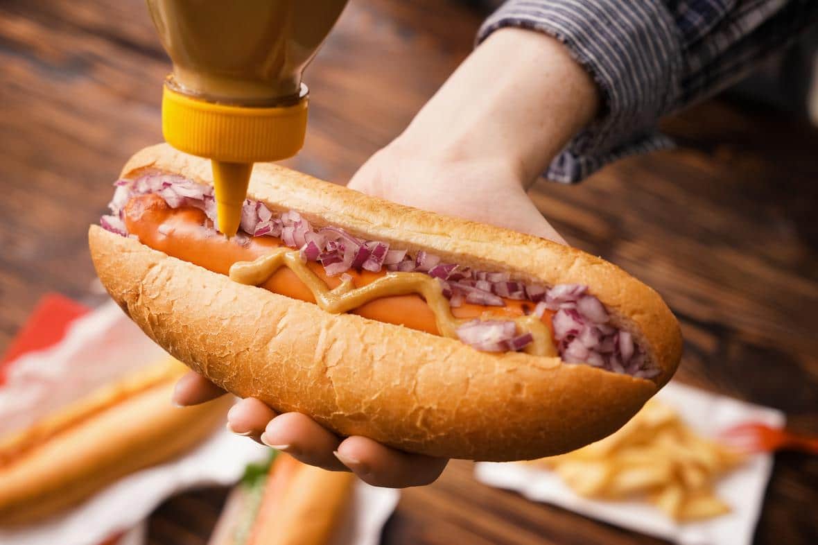 A soy protein hot dog with toppings being offered on a plate