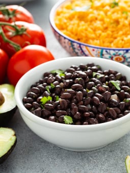 A bowl of black beans next to tomatoes and Mexican rice