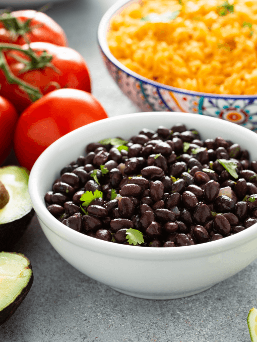 A bowl of black beans next to tomatoes and Mexican rice