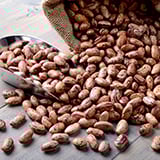 An overflowing burlap sack of pinto beans next to a metal scoop