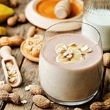 A glass of peanut butter banana smoothie surrounded by peanut shells