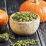 A bowl of seeds next to pumpkins