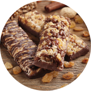 Three plant based chocolate protein bars on a wooden table with dried raisins sprinkled around them.