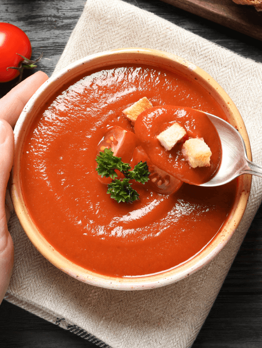 A spoon being lifted out of a bowl of rich red tomato soup