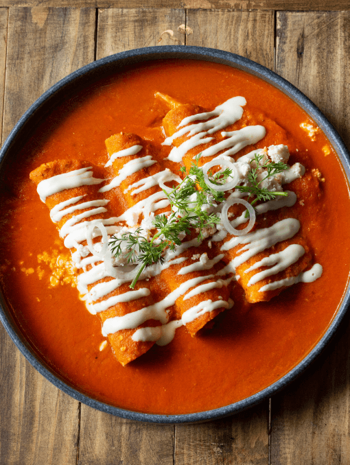 A bowl of enchiladas smothered in a deep red sauce