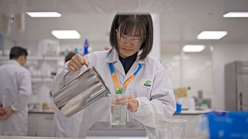 A scientist in a lab pours liquid into a testing vessel 