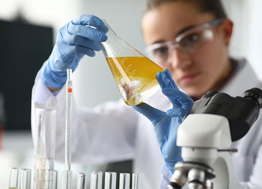 A person holding a beaker with yellow liquid